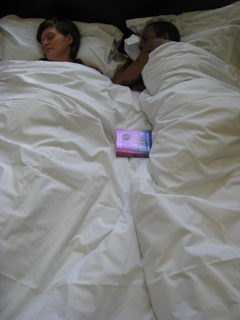 A couple lie sleeping in bed, between them, above the sheets, is Eckhart Tolle's book, 'A New Earth'